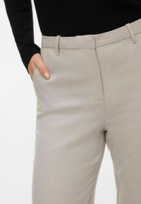 Beige skreddersydde bukser med teksturert finish, med flatt forstykke og sidelommer, kombinert med en tettsittende svart langermet topp.