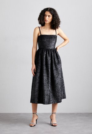 Sort sansærmet kjole med en tætsiddende overdel og en svungen nederdel, lavet af struktureret stof med en subtil glans. Har tynde stropper og en længde til midt på læggen.