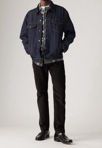 Jeansjacka i mörkblått med silverdetaljer, lager-på-lager över en grön rutig skjorta. Svarta manchesterbyxor och svarta skor fulländar looken.