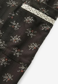 Material negru cu un model floral în alb și portocaliu. Prezintă un tăietor din dantelă și o suprafață texturată. O buzunar vizibil la margine.