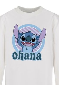 Hvid langærmet skjorte med en cartoonfigur med blå hud og store ører, omgivet af en rund blå og pink grafik, der inkluderer ordet "ohana."