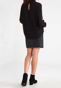 Blouse noire à manches longues avec un détail à l'encolure en goutte d'eau dans le dos, assortie à une jupe grise et des bottines noires à talon bloc.