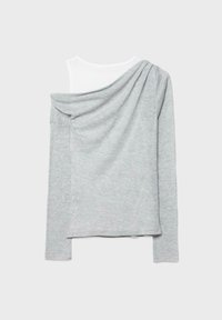 Haut gris clair à manches longues avec un drapé asymétrique tombant sur une épaule, superposé à un vêtement intérieur blanc sans manches.