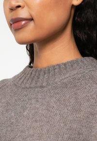 Gray knit sweater with a ribbed neckline, featuring a soft texture and a casual silhouette, partially visible on a model's shoulder and neck.