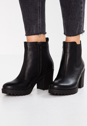 Sorte læder-ankelstøvler med et slankt design, udstyret med en sidelås, chunky hæle og teksturerede gummisåler for bedre greb.