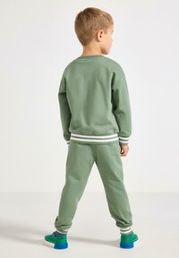 Zestaw zielonego bawełnianego swetra i spodni z białymi paskami na mankietach i pasie. Spodnie mają luźny krój i zwężają się przy kostkach.