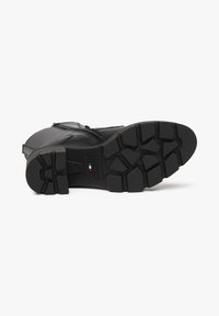 Black leather boot with a rugged rubber sole featuring deep treads and a side zip closure. Flat heel and smooth texture.