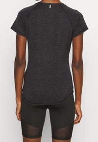 Mörkgrå atletisk tröja med korta ärmar, rundad fåll och en liten etikett vid halslinningen, kombinerad med svarta shorts med genomskinliga detaljer.