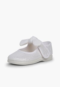 White perforated shoe with a rounded toe, secure strap, and a bow detail on top. Textured upper and smooth sole design.