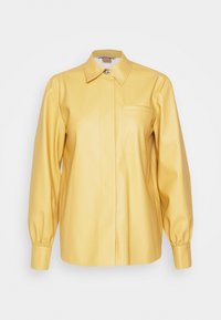 Chemise jaune en simili cuir à manches longues avec col pointu, une poche poitrine, poignets boutonnés et boutons dissimulés sur le devant.