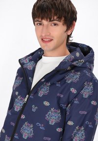 Jachetă cu glugă din țesătură bleumarin, având un model grafic colorat cu flori și creaturi. Fermuar frontal și mansete elastice pentru un fit confortabil.