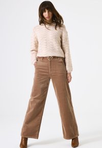 Beige gebreide trui met golfpatroon, gecombineerd met wijde bruine corduroy broek en een bruine riem met een gouden dubbele cirkelgesp.