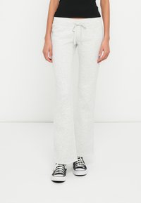 Ανοιχτό γκρι φαρδιά φόρμα με κορδόνι στη μέση, κατασκευασμένη από απαλό ύφασμα, σετ με μαύρα και λευκά αθλητικά παπούτσια.