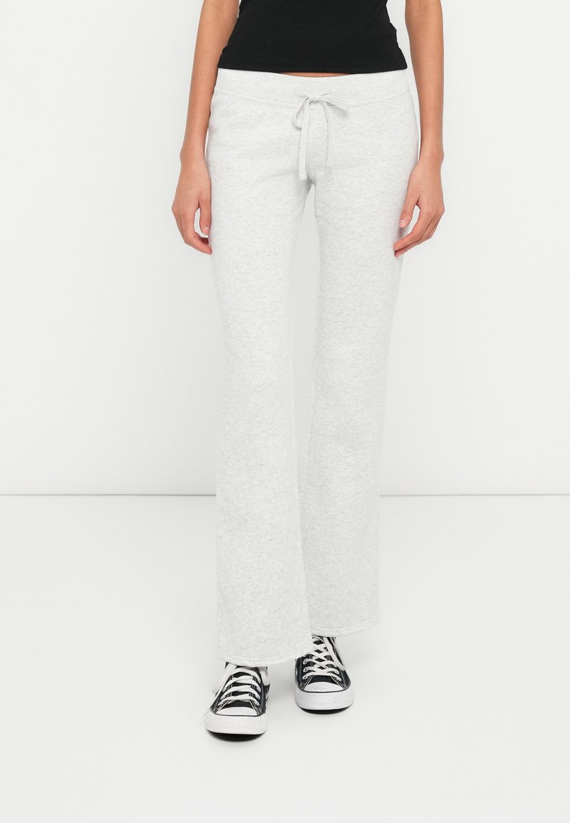 Ανοιχτό γκρι φαρδιά φόρμα με κορδόνι στη μέση, κατασκευασμένη από απαλό ύφασμα, σετ με μαύρα και λευκά αθλητικά παπούτσια.