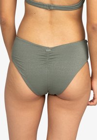 Mörkgrön bikiniunderdel med en glänsande textur, prydd med en rynkad detalj på baksidan. Enkelt design, utan ytterligare mönster eller metall detaljer.