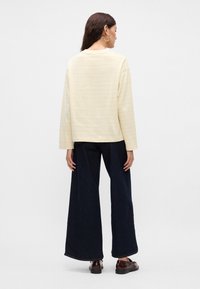 Μακρυμάνικο ανοιχτό κίτρινο ριγέ μπλουζάκι συνδυασμένο με φαρδιά τζιν παντελόνια σε σκούρο χρώμα. Τα χαρακτηριστικά περιλαμβάνουν στρογγυλή λαιμόκοψη και απλή βαμβακερή υφή.