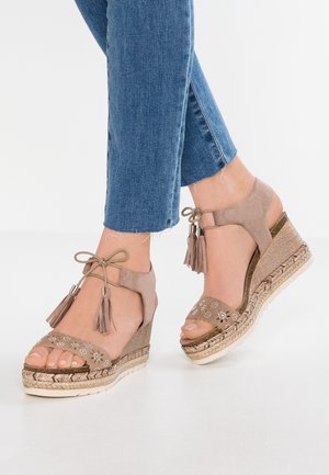 Kilesandaler med beige ruskindsoverdel, dekoreret med blomsterudskæringer og pynt, med et kvastaccent og flettet jutesål.