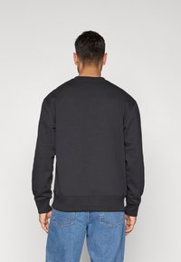 Felpa nera con scollo rotondo e polsini a costine, indossata al contrario. Abbinata a jeans di jeans blu, con una vestibilità comoda.