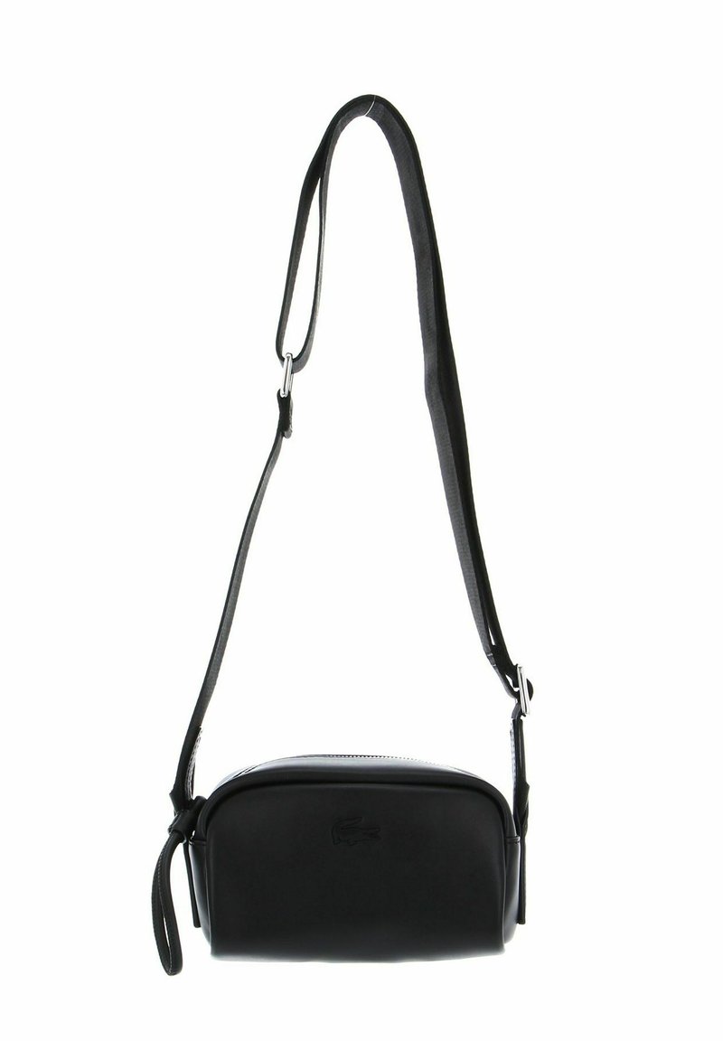Bolso cruzado de piel negra con textura suave, forma redondeada, correa ajustable y herrajes en color plata. Logo de Lacoste grabado en la parte frontal.