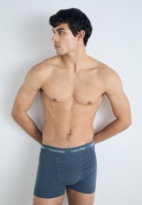 Men's boxer briefs in dark blue fabric with a smooth texture. Features a Calvin Klein logo waistband and a fitted design.