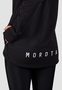 Čierna mikina so zúženými manžetami, so bočným zipsom a bielym označením "MOROTAI" na spodnej časti. Hladký materiál s priliehavým dizajnom.