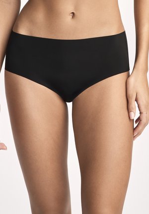 Frau trägt nahtlose schwarze Hipster-Unterwäsche, gezeigt von der Taille bis zur Mitte des Oberschenkels vor neutralem Hintergrund.