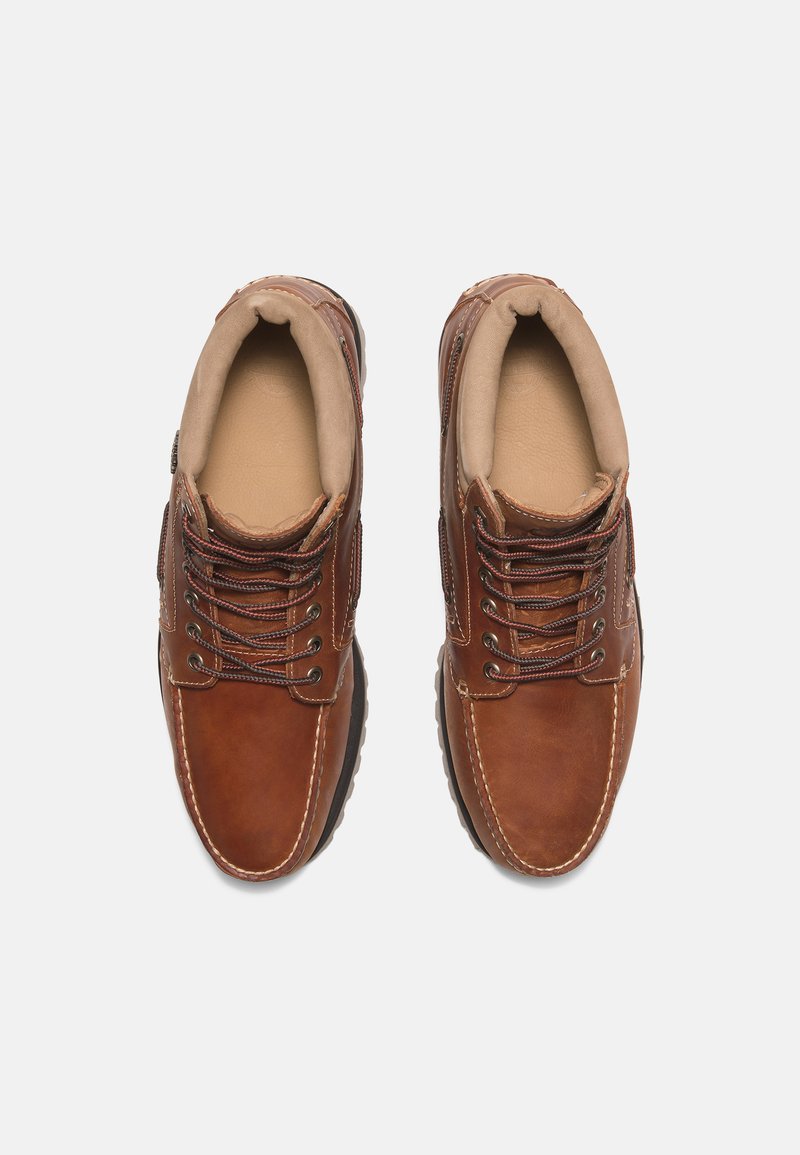 Brązowe skórzane buty z okrągłym noskiem, wyściełanym kołnierzem i sznurowanym przodem. Posiadają przeszycia i gumową podeszwę zapewniającą przyczepność.