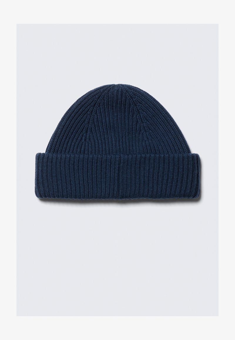 Bonnet en laine tricotée bleu foncé avec un revers, présenté à plat sur un fond gris clair.