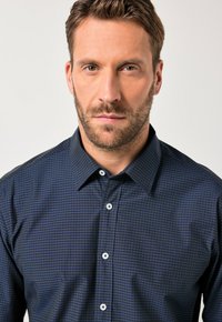 Tmavě modrá kostkovaná košile s límečkem na knoflíky, zdobená bílými knoflíky a texturovanou tkaninou. Design obsahuje jemný mřížkovaný vzor.