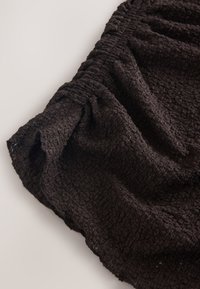 Jupe en tissu noir texturé avec une taille élastique froncée, présentant un motif tissé et une surface douce et froissée.