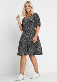 Mustana mekko, jossa on valkoisia spiraali- ja kukkakuoseja, lyhyet hihat, V-pääntie, kellotettu hame, yhdistetty valkoisiin tennareihin. Silkkinen kangaspinta.