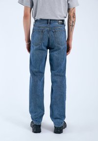 Jeans de mezclilla azul añil, de corte holgado con cintura alta, dos bolsillos traseros y una etiqueta en la cinturilla. La tela tiene una textura resistente.