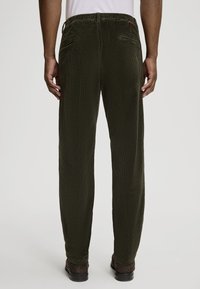 Pantalons en velours côtelé vert foncé avec une coupe décontractée, dotés d'une ceinture et de deux poches arrière, tissu texturé avec des côtes visibles.