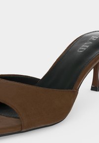 Escarpin marron à bout ouvert avec semelle intérieure noire et le nom de la marque "P.A.N.D" visible sur la zone du talon.