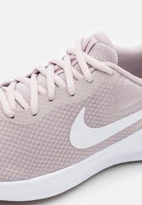 Baskets de sport roses claires avec une tige en maille, un swoosh blanc accrocheur, un bout arrondi et des lacets plats. Surface texturée et col rembourré pour le confort.