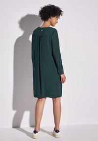 Robe verte à manches longues avec une coupe ample, dotée d'un empiècement froncé et d'un petit détail de bouton à l'arrière. Tissu doux et léger.