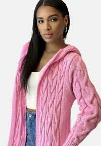 Jasnoróżowy dziany kardigan z kapturem, z wzorem warkoczowym, długimi rękawami i otwartym przodem; miękka tekstura.