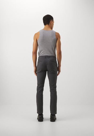 Débardeur gris porté avec un pantalon ajusté gris foncé ; le pantalon présente des poches latérales et un design de jambe effilée. Fond uni.