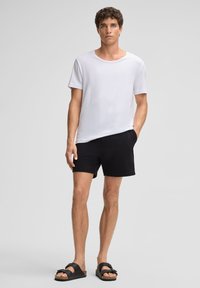Witte katoenen t-shirt met een ronde halslijn, gecombineerd met zwarte gewatteerde short en zwarte schuifslippers met banden over de voet.