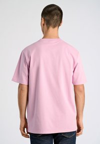 Rosa kortärmad t-shirt, tillverkad av bomullstyg, med rund hals och avslappnad passform, bärs med mörka jeans, enkel bakvy.
