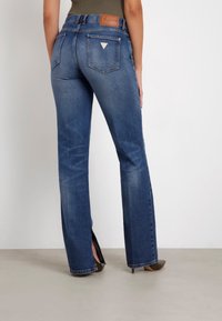 Laia sinise denimi pükse, millel on kõrge vöökoht, tagakotid ja pruun nahkpatch vöö peal. Sile tekstuur ja kerge pleekimine.