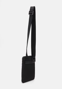 Černá crossbody taška s elegantním obdélníkovým tvarem, vyrobená z hladké tkaniny a vybavená zipovým uzávěrem a nastavitelným popruhem.
