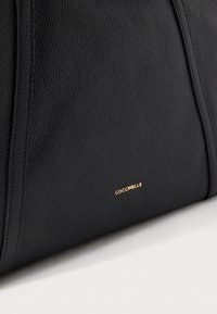 Borsa nera in pelle con finitura testurizzata, caratterizzata da dettagli in oro e il nome del marchio "Goccinelle" impresso sul lato.