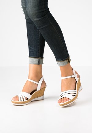 White wedge sandals with cross strap design, textured tan cork wedge heel, adjustable ankle strap, and white rubber sole.
