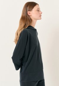 Felpa con cappuccio grigia scura a maniche lunghe, dal taglio rilassato, con un collo alto e una leggera texture. Spalle senza cuciture e fessure laterali.