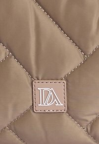 Tela de nailon marrón acolchada con un patrón diagonal y un parche de logo cuadrado en color beige claro con letras blancas.