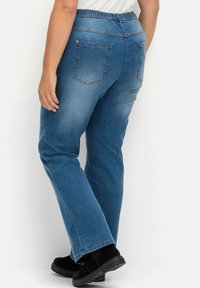 Vaqueros de mezclilla azul con cintura elástica, corte recto y dos bolsillos traseros. La tela tiene una textura suave y un ligero desvanecimiento.