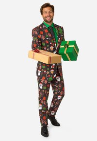 Krāsains svētku uzvalks ar melnu fona, kurā redzami svētku raksti ar dāvanām, piparkūku cilvēciņiem un sniegavīriem. Modelis tur divas iesaiņotas dāvanas.