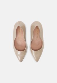 Beżowe lakierowane szpilki ze spiczastym noskiem o gładkim wykończeniu, z wyściółką amortyzującą i subtelnym logo wewnątrz buta.