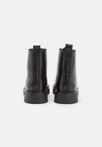 Botas de cuero negro hasta el tobillo con un acabado suave, que cuentan con una suela plana y un detalle de logo grabado en la parte posterior. Diseño minimalista sin acentos adicionales.